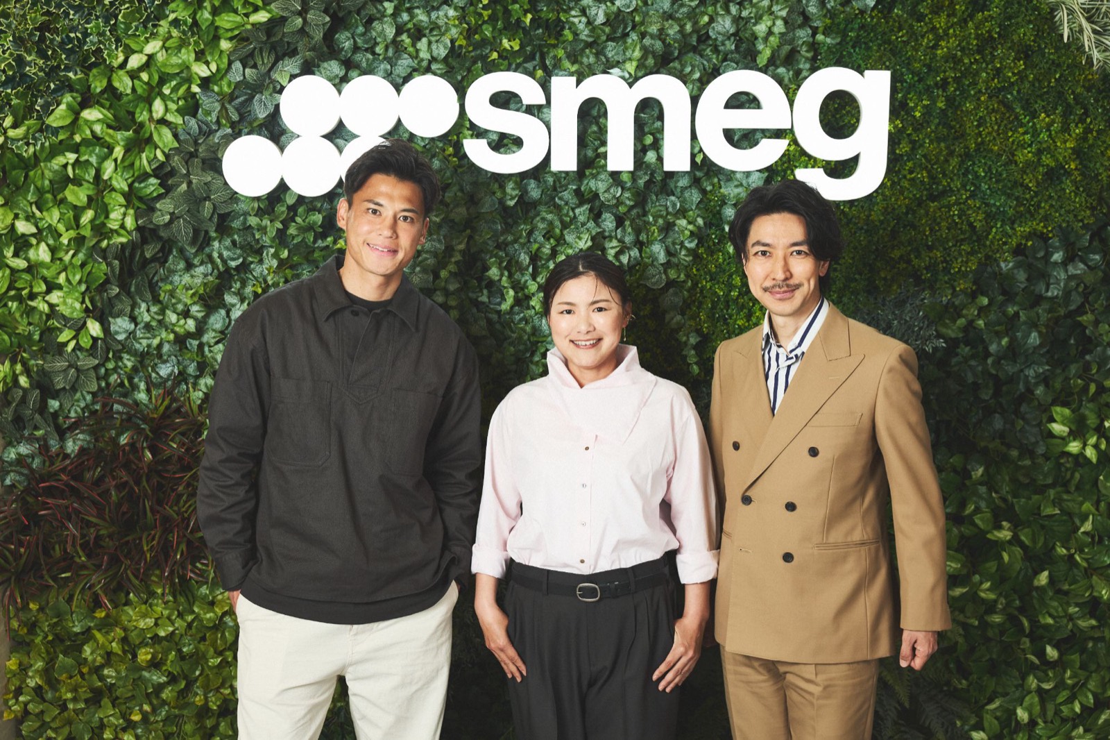 smegのロゴが掲げられた緑の壁の前に並ぶ、アンバサダーに就任した横峯さくら、TAKAHIROさん、宮市亮さんの3人